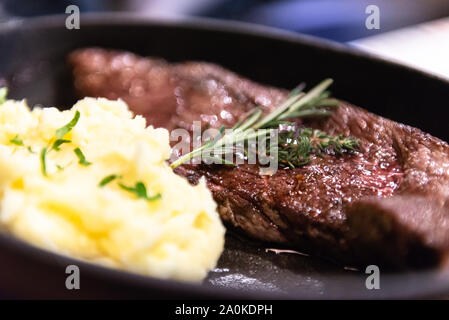 Bistecca di manzo con le patate in una pentola. Il rosmarino sulla carne fritta. Foto Stock