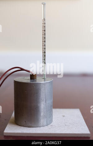 Capacità di calore specifico di esperimento di alluminio impostare senza isolamento. Il blocco di alluminio con un riscaldatore ad immersione e termometro su un tappetino resistente al calore Foto Stock