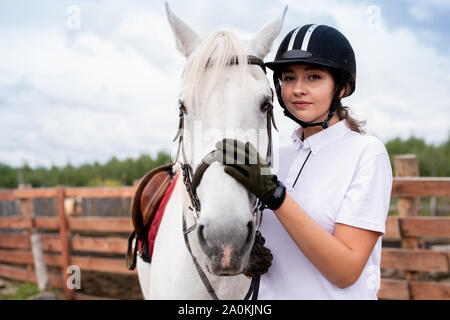 Calma la donna in bianco Polo shirt e abbigliamento equestre abbracciando cavallo di razza pura Foto Stock