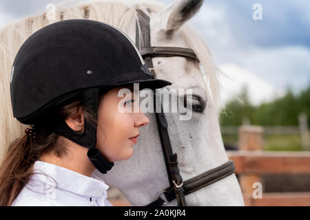 Profilo di giovane donna attiva nel casco equestre e bianco cavallo di razza pura Foto Stock