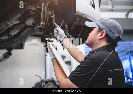 Maschio asiatici auto auto tecnico di manutenzione per i clienti in base al veicolo specificati. Lista di controllo per la manutenzione. Il disco di usura pastiglie freni riparazione automobilistica Foto Stock