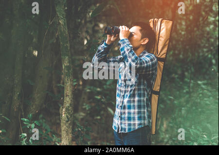 L'uomo con il binocolo telescopio nel bosco alla ricerca destinazione come perso persone o in un futuro prevedibile. La gente di stili di vita e attività di svago di concetto. Natu Foto Stock