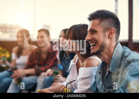 Un gruppo di giovani persone sorridenti di bere un cocktail e rilassarsi sulla terrazza sul tetto al tramonto. Il concetto di amicizia Foto Stock