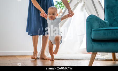 Madre aiutare Baby figlio di prendere i primi passi a casa Foto Stock