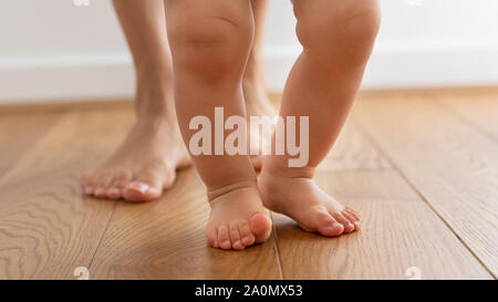 Close Up di madre aiutare Baby figlio di prendere i primi passi a casa Foto Stock