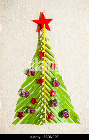 Albero di Natale fatto di verde palm te brunch con piccolo rosso decorazioni di festa sulla sabbia, vista dall'alto, composizione verticale Foto Stock