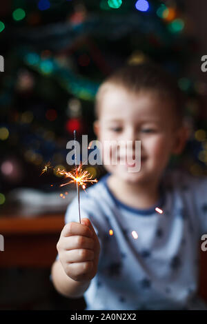 Splendido piccolo bambino holding burning sparkler per la Vigilia di Capodanno, bengala fire. Selezionare la messa a fuoco sui fuochi d'artificio. Foto Stock