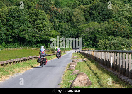 Merthyr Tydfil, Wales, Regno Unito - 18 Luglio 2019: una coppia di cicloturisti ride passato west calder serbatoio sul ciclo nazionale di instradamento di rete 8 in Brecon Bea Foto Stock