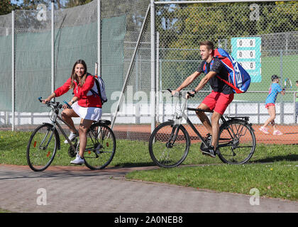 Coppia giovane in bicicletta tra i tribunali del loro tennis club Foto Stock