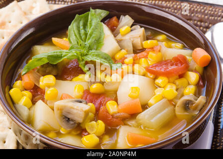 In casa calda zuppa di verdure e servito con croccante saltine cracker in una ciotola marrone. Foto Stock