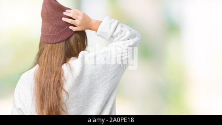 Giovane bella bruna hipster donna che indossa occhiali e cappello invernale su sfondo isolato indietro pensando di dubbio con la mano sulla testa Foto Stock