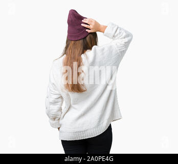 Giovane bella bruna hipster donna che indossa occhiali e cappello invernale su sfondo isolato indietro pensando di dubbio con la mano sulla testa Foto Stock