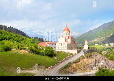 Chiesa di San Nicola sul colle verde delle montagne sullo sfondo in Mestia, Georgia Foto Stock