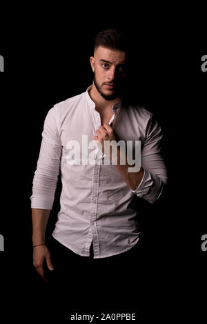 Riflessivo bruna giovane uomo in camicia bianca pensando a qualcosa di isolato su uno sfondo nero. Foto verticale. Foto Stock