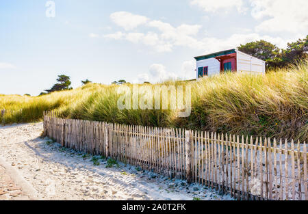 Una piccola spiaggia in legno cottage, parzialmente nascosto da graminacee selvatiche dietro una staccionata in legno, sporgente al di sopra delle dune su una soleggiata mattina d'estate. Foto Stock
