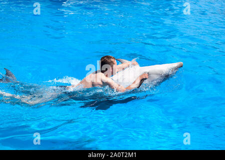 Un giovane uomo è cavalcare dolphin, ragazzo di nuoto con dolphin sul retro in blu acqua nella piscina di acqua di mare, l'oceano, Dolphin salva un uomo Foto Stock