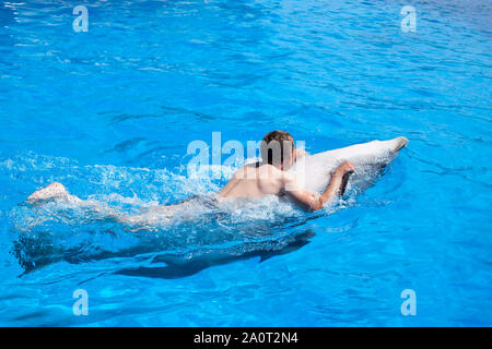 Un giovane uomo è cavalcare dolphin, ragazzo di nuoto con dolphin sul retro in blu acqua nella piscina di acqua di mare, l'oceano, Dolphin salva un uomo Foto Stock