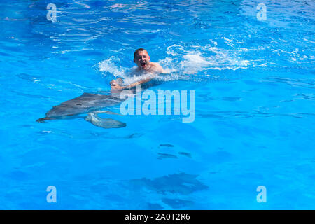 Un giovane uomo è cavalcare dolphin, ragazzo di nuoto con Delfino Blu in acqua nella piscina di acqua di mare, l'oceano, Dolphin salva un uomo Foto Stock