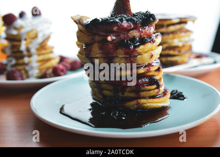 Pancake con marmellata di gocciolamento su una piastra di colore blu con i lamponi. Foto Stock