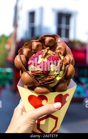 Sorbetto al pistacchio in una cialda di cacao guarnita con le noci pecan e lamponi da Bubblewrap gelateria, Chinatown, London, Regno Unito Foto Stock