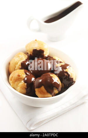 Profiteroles contemplati in una ricca salsa di cioccolato servito in un bianco ciotola da dessert Foto Stock