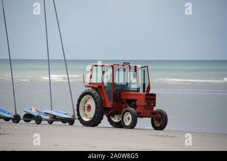 Un trattore tirando 9 collegati sabbia yachts, senza vele, sulla spiaggia in preparazione di un concorso Foto Stock