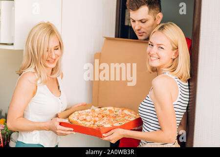 Corriere consegna pizza ai clienti home. Due lieti gioiosa giovane donna soddisfatto con la consegna della pizza, essi ridendo e cercando di fotocamera. Il Pizz Foto Stock