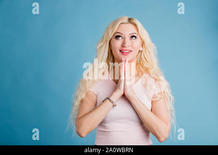 Bella donna bionda sorride e chiude gli occhi e la supplica per la meglio su sfondo blu Foto Stock