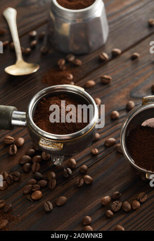Portafilters vicino geyser macchinetta per il caffè e il cucchiaio sul buio superficie in legno Foto Stock
