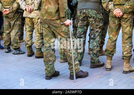 Un soldato ferito dell'esercito ucraino in uniforme stand con una stampella vicino la formazione dei veterani di guerra, Defender Ucraina giorno. Forze armate di Ukra Foto Stock