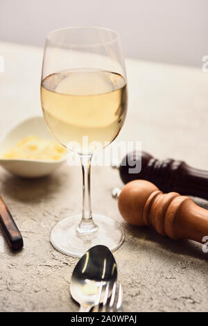 Vista ravvicinata di vetro con vino bianco nei pressi di pepe e sale di mulini e formaggio grattugiato isolato su grigio Foto Stock