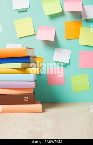 Pila di libri sul tavolo vicino a variopinti sticky notes sulla parete turchese Foto Stock