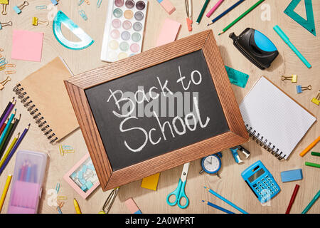 Vista superiore di varie forniture scolastiche e lavagna con il ritorno a scuola di scritte sulla scrivania in legno Foto Stock