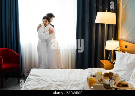 Messa a fuoco selettiva di uomo bello e attraente brunette donna abbracciando nella camera di albergo Foto Stock