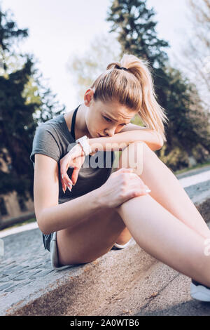 Triste feriti sportive di piangere mentre è seduto sul marciapiede di confine Foto Stock