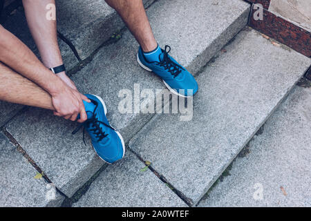 Ritagliato colpo di uomo in sneakers seduti sulle scale e toccando la gamba infortunata Foto Stock