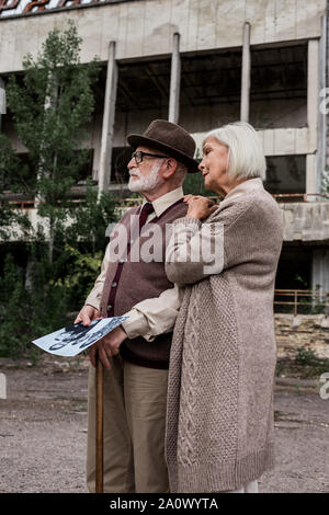 Pripjat, Ucraina - Agosto 15, 2019: si ritira l uomo e la donna azienda foto in bianco e nero vicino all'edificio Foto Stock