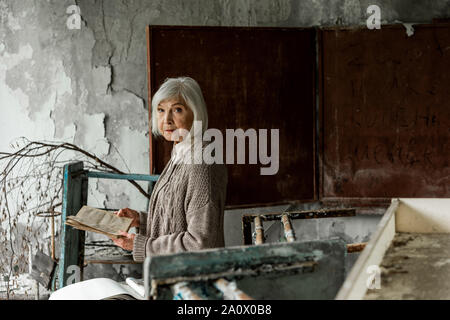 Ritirato donna con i capelli grigi azienda prenota in mani vicino a Chalk board Foto Stock