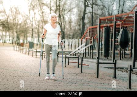 Vecchia età ridendo donna facendo Nordic walking sul campo sportivo Foto Stock