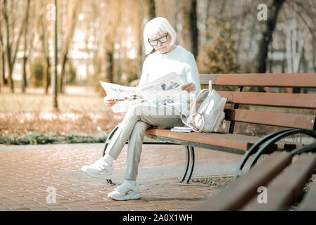 Avvenenti senior dame absorbedly leggendo il giornale nel parco Foto Stock