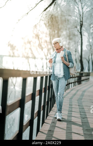 Grigio pacifica dai capelli donna in cuffia percorrendo a piedi il parco Foto Stock