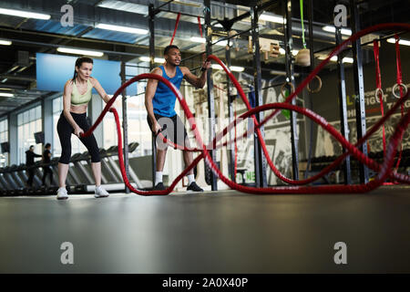 Ampio angolo ritratto di montare la coppia giovane esercitando con funi di battaglia durante l'allenamento di resistenza in croce palestra funzionale, spazio di copia Foto Stock