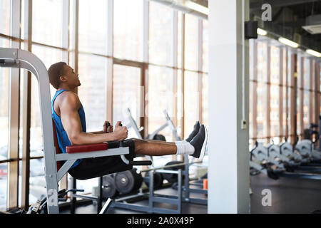 Vista laterale verticale della muscolatura afro-americano di uomo con macchine per esercizi durante gli allenamenti in palestra moderna contro la finestra spazio di copia Foto Stock