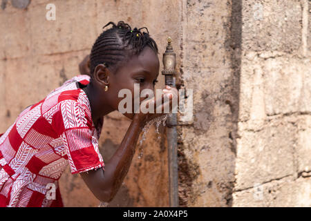 Ritratto della bella ragazza africana di bere da un rubinetto