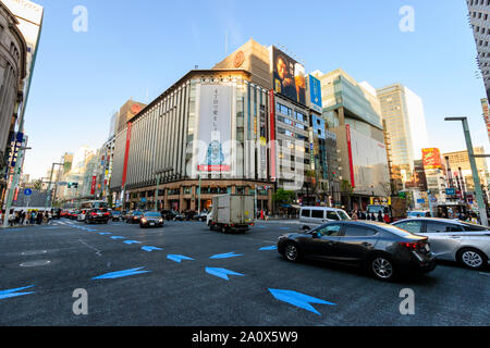 Tokyo, il Ginza 4 interscambio con traffico verso il passato e flagship Mitsukoshi department store di fronte. Ora d'oro, nel tardo pomeriggio. Blue sky. Foto Stock