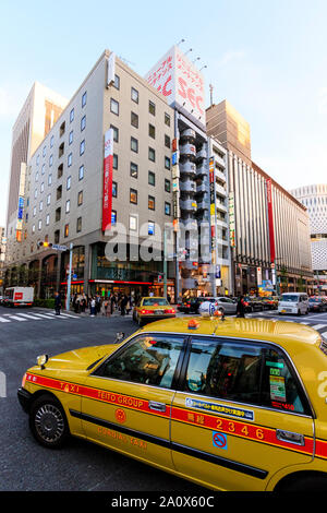 Tokyo. Primo piano, giallo taxi passando da a Ginza 3 intersezione e attraversamento pedonale con il Mitsukoshi store e altri di fronte. Foto Stock