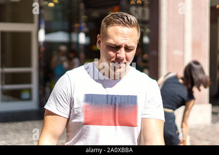 Preoccupato giovane uomo in T-shirt casual camminando in una strada urbana guardando giù accigliata a se stesso come egli cammina Foto Stock