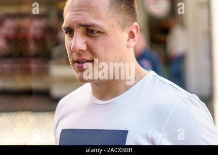 Considerato giovane uomo in T-shirt casual camminando in una strada urbana con un look pensieroso Foto Stock