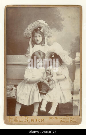 Originale edoardiano antico cabinet card, affascinante studio ritratto di tre giovani fratelli graziosi, sorelle, in abiti estivi, con grandi cappelli di paglia e camici bianchi, dallo studio di Herbert e James Rigden, Bowes Park, Londra, Regno Unito circa 1904. Foto Stock