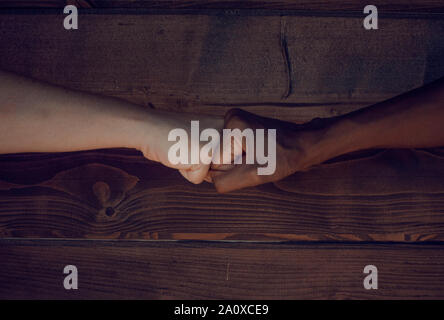 Pugno di bump due donne (nero e caucasica) su uno sfondo di legno Foto Stock